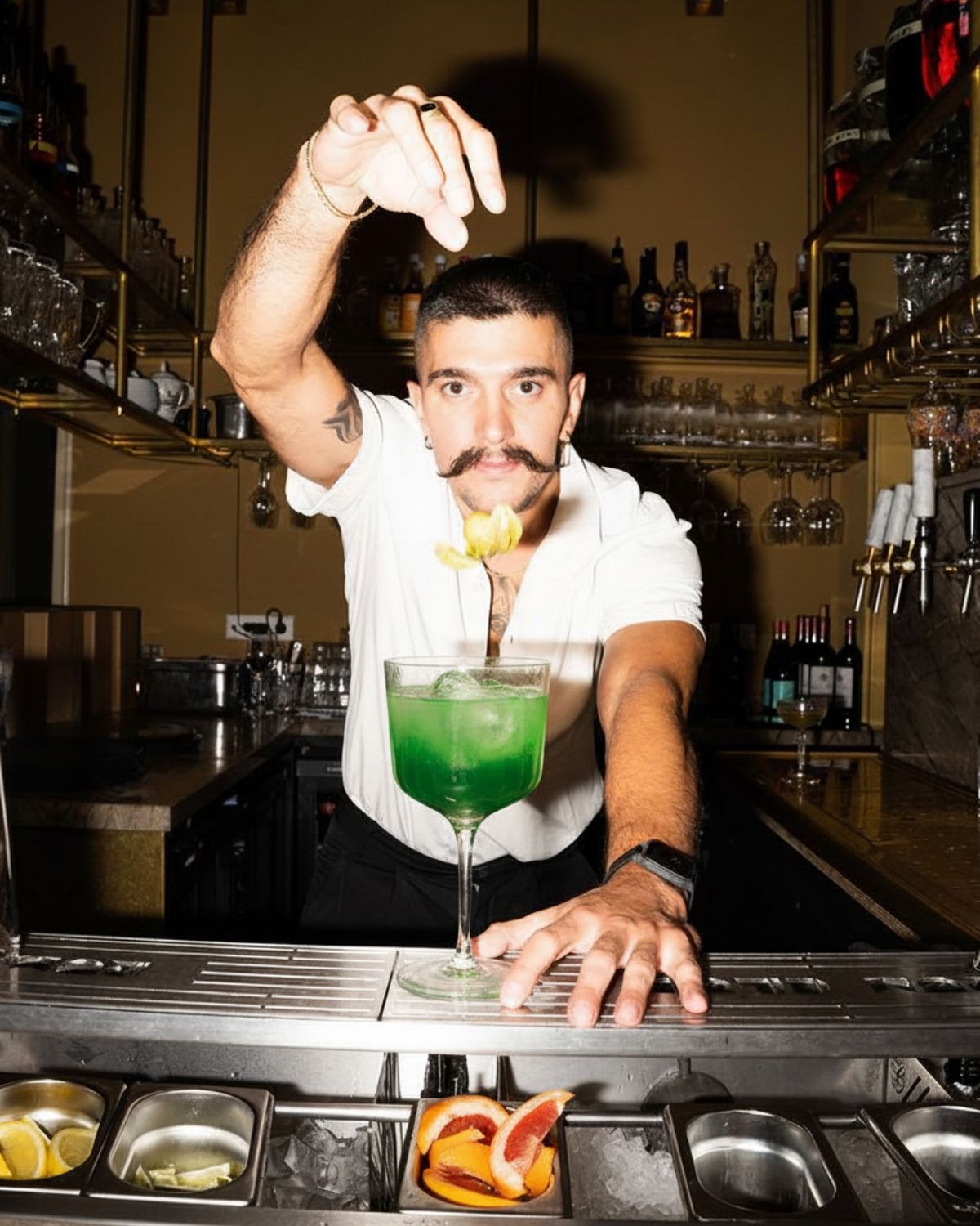 Bartender dropping a garnish into a green cocktail