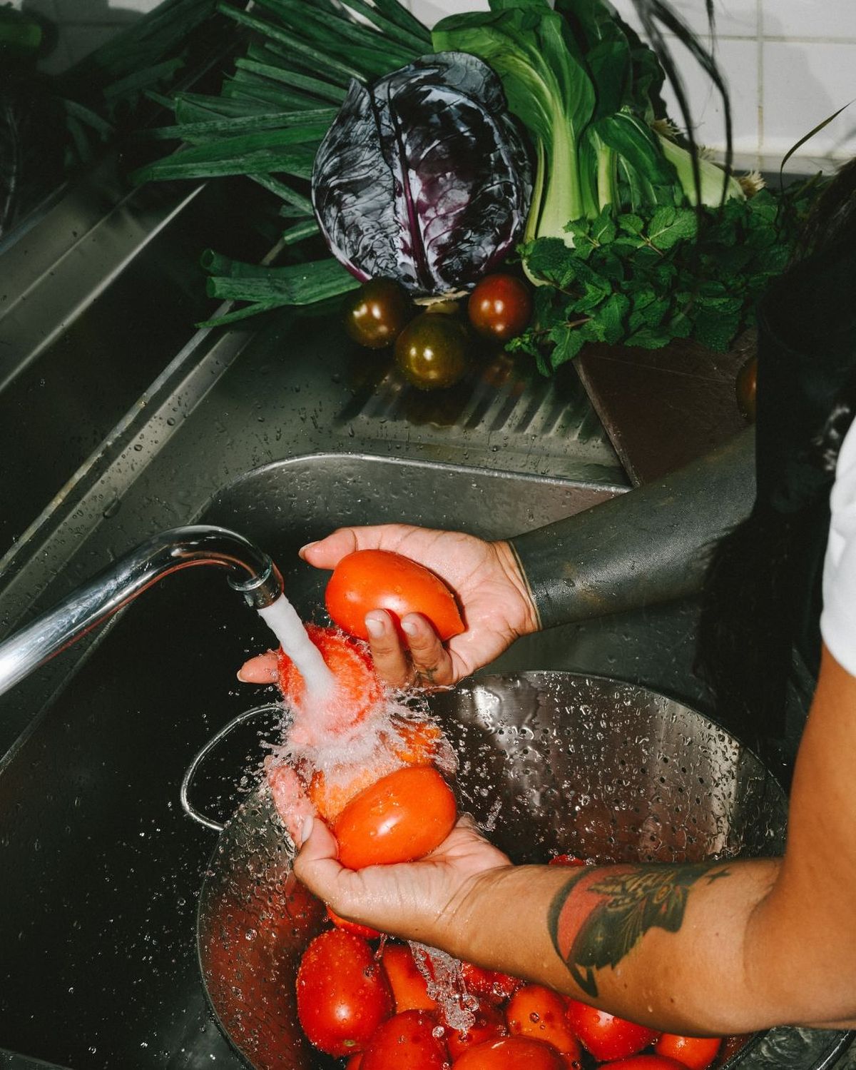 Hands washing fresh tomatoes in a kitchen sink